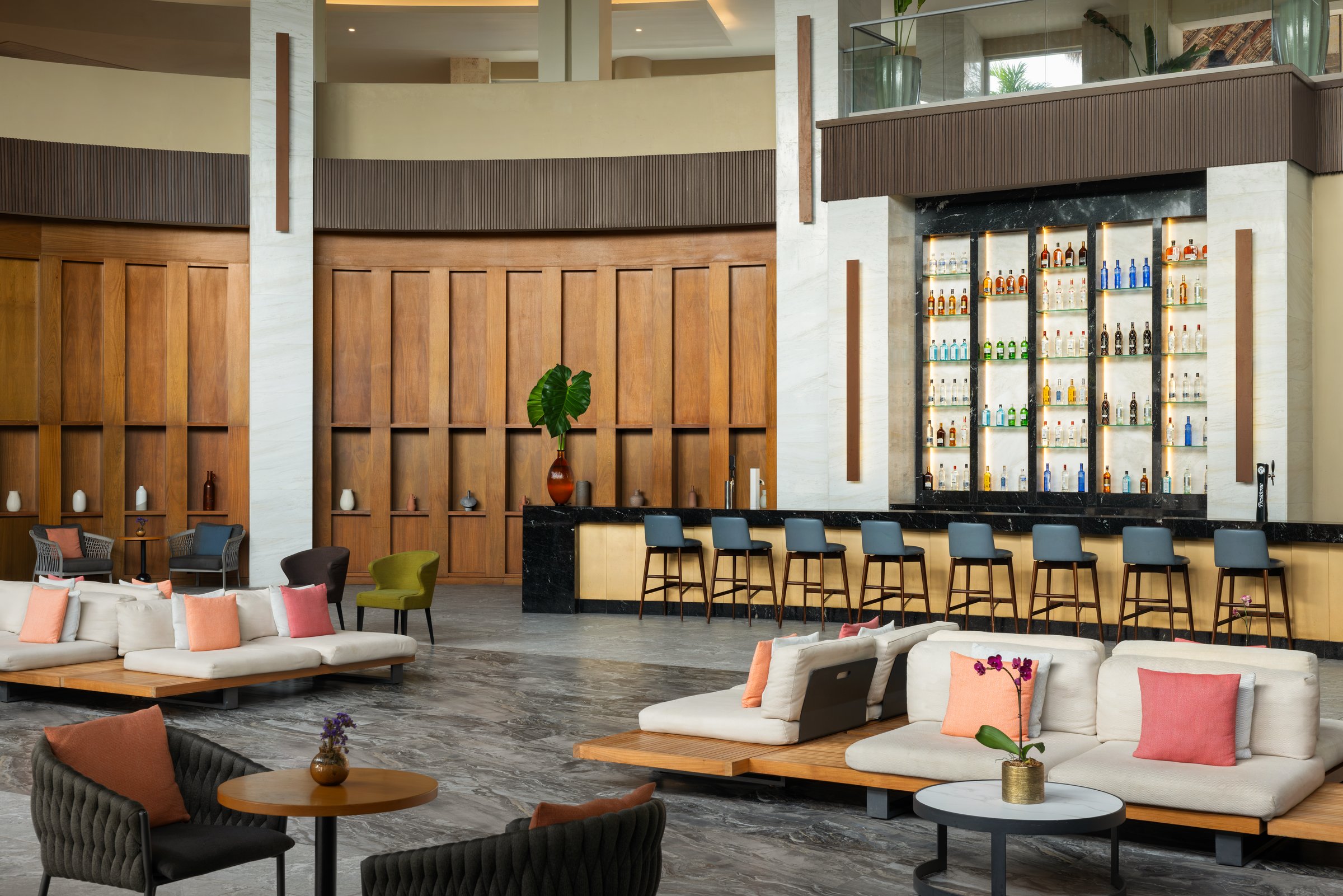 Closer view of the Wink lobby bar counter with black stools, a backlit bottle wall and low tables with flower arrangements.