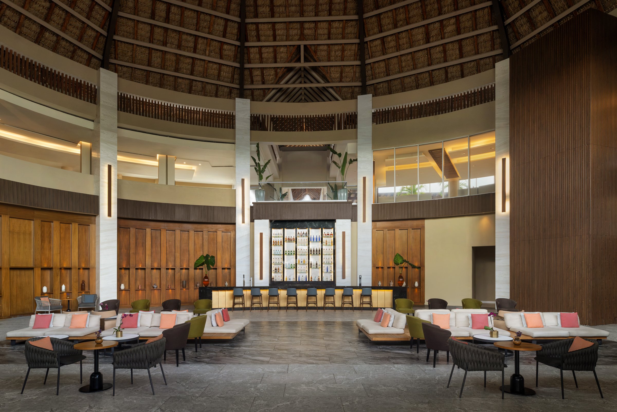 Wink lobby bar in a round room under a high thatched-style ceiling, with white sofas, pink and orange pillows and a lit bottle display.