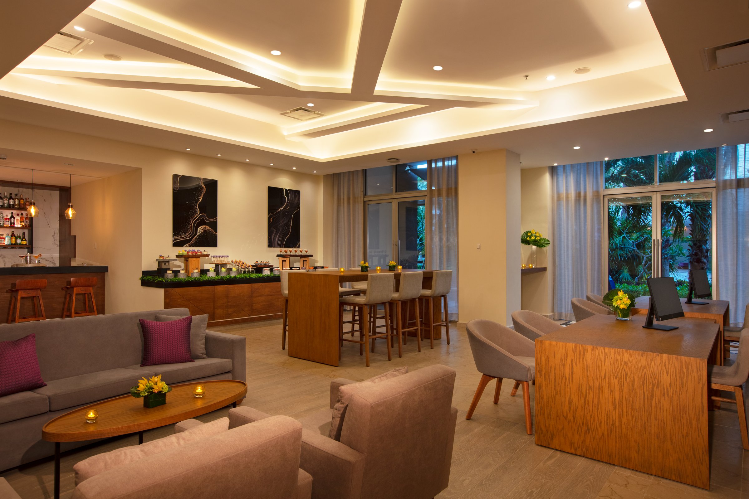 Xcelerate lounge with gray sofas, light wood tables, a bar area and large windows letting in daylight.