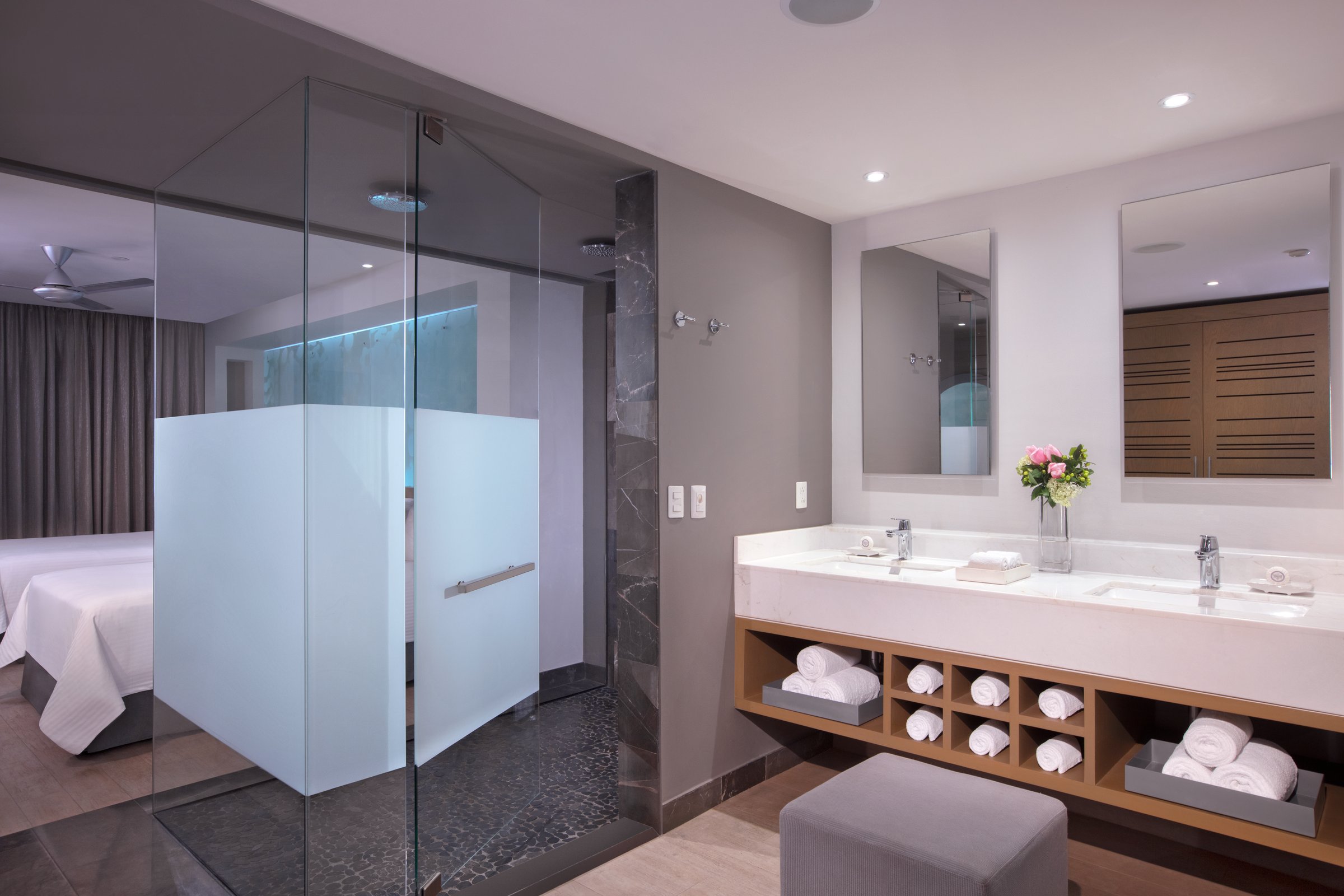 Junior suite bathroom with a double vanity, two rectangular mirrors, white sinks and a glass-walled shower.