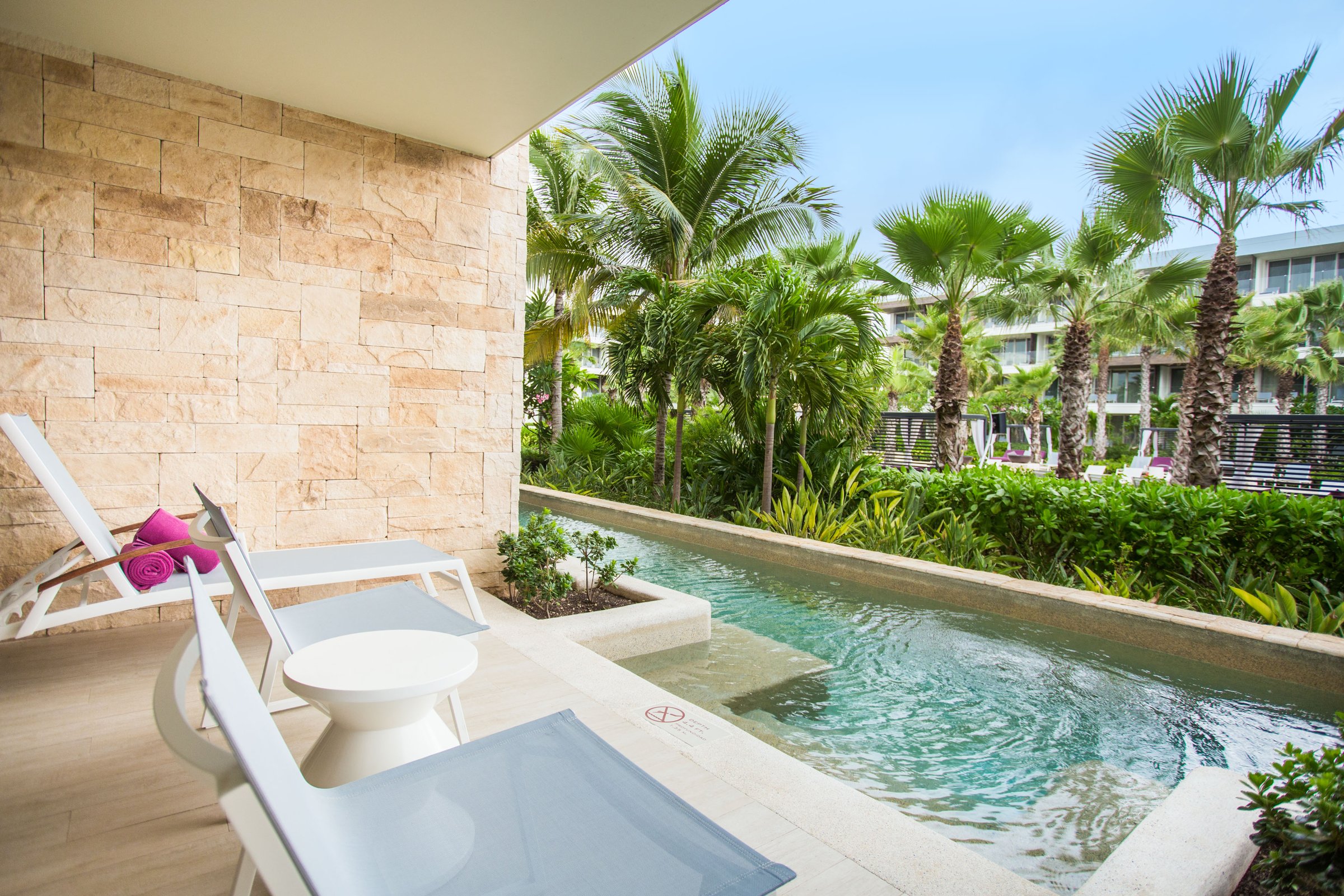 Ground-floor suite terrace with a built-in plunge pool, white loungers and a stone wall among tropical plants.