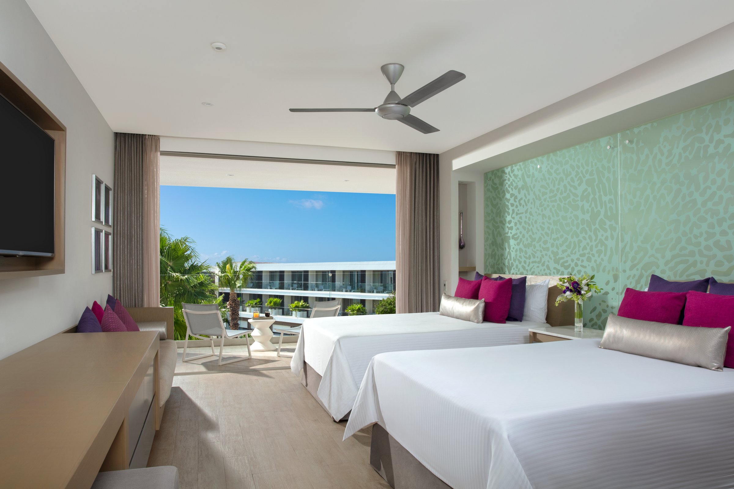 Allure junior suite with two double beds, white linens and purple pillows, and a sliding door to a balcony under a clear blue sky.