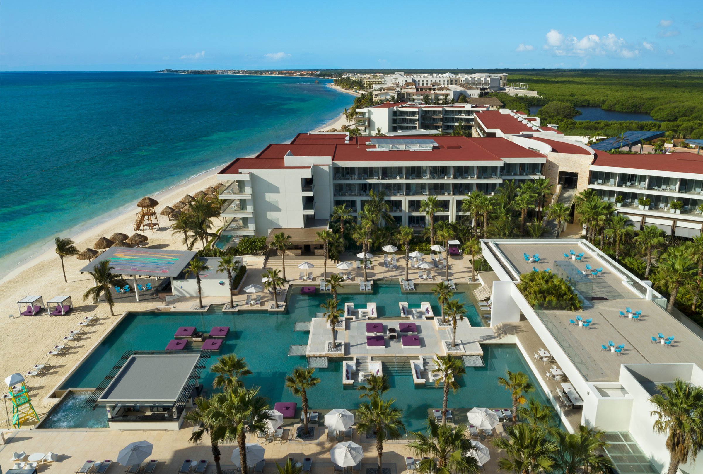 High-angle view of the Energy Pool with square islands of white loungers and purple pillows, palms and the beach at left.