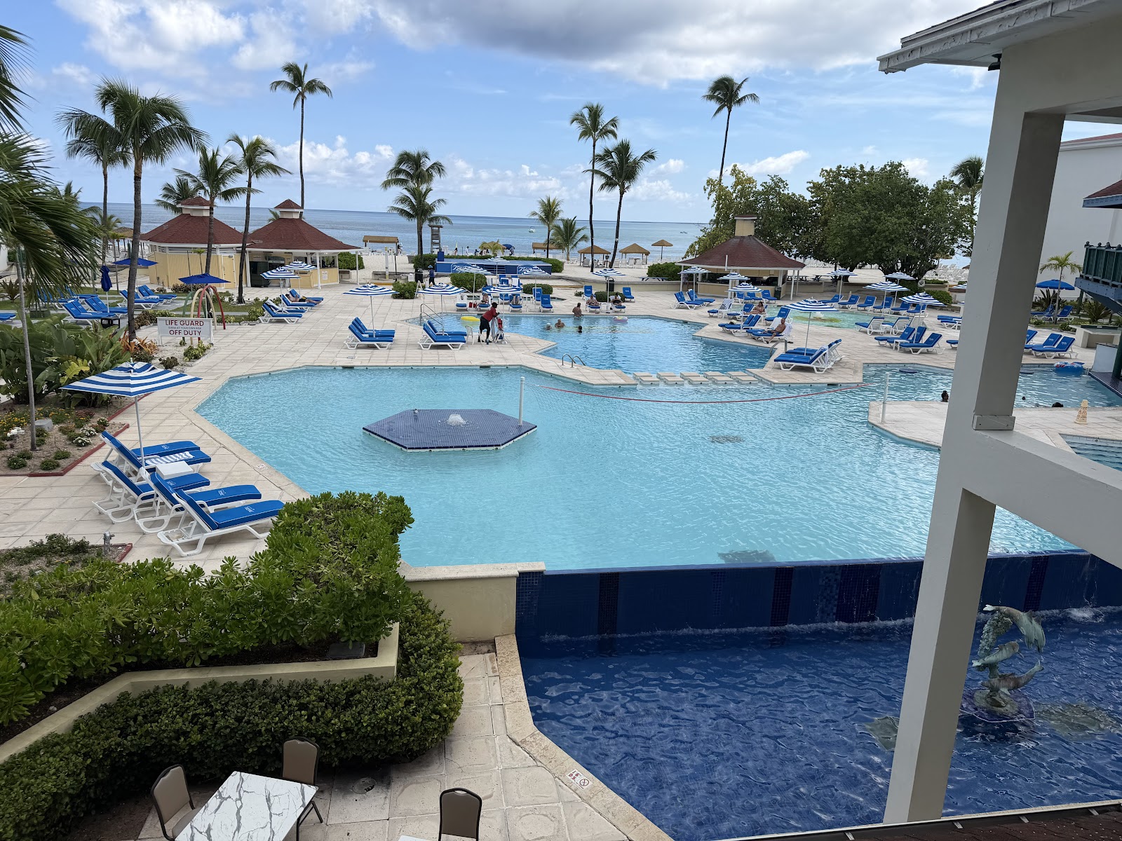Multiple swimming pools with blue loungers, palm trees, and turquoise ocean beyond at Breezes Resort Bahamas.
