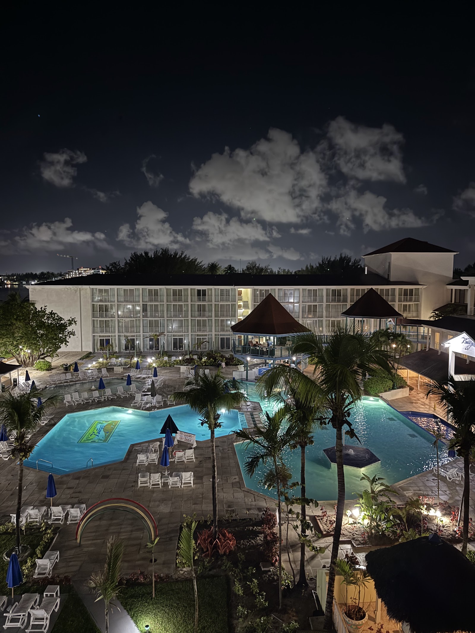 Nighttime view of Breezes Resort Bahamas with illuminated pools, palm trees, lounge chairs, and main building under a starlit sky.
