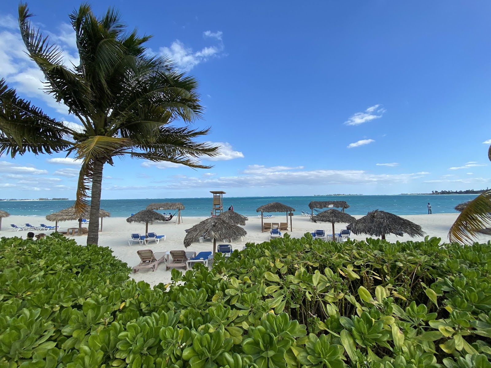 Thatched-roof swings and wooden cabana frame a turquoise lagoon and white sand beach at Breezes Resort Bahamas.