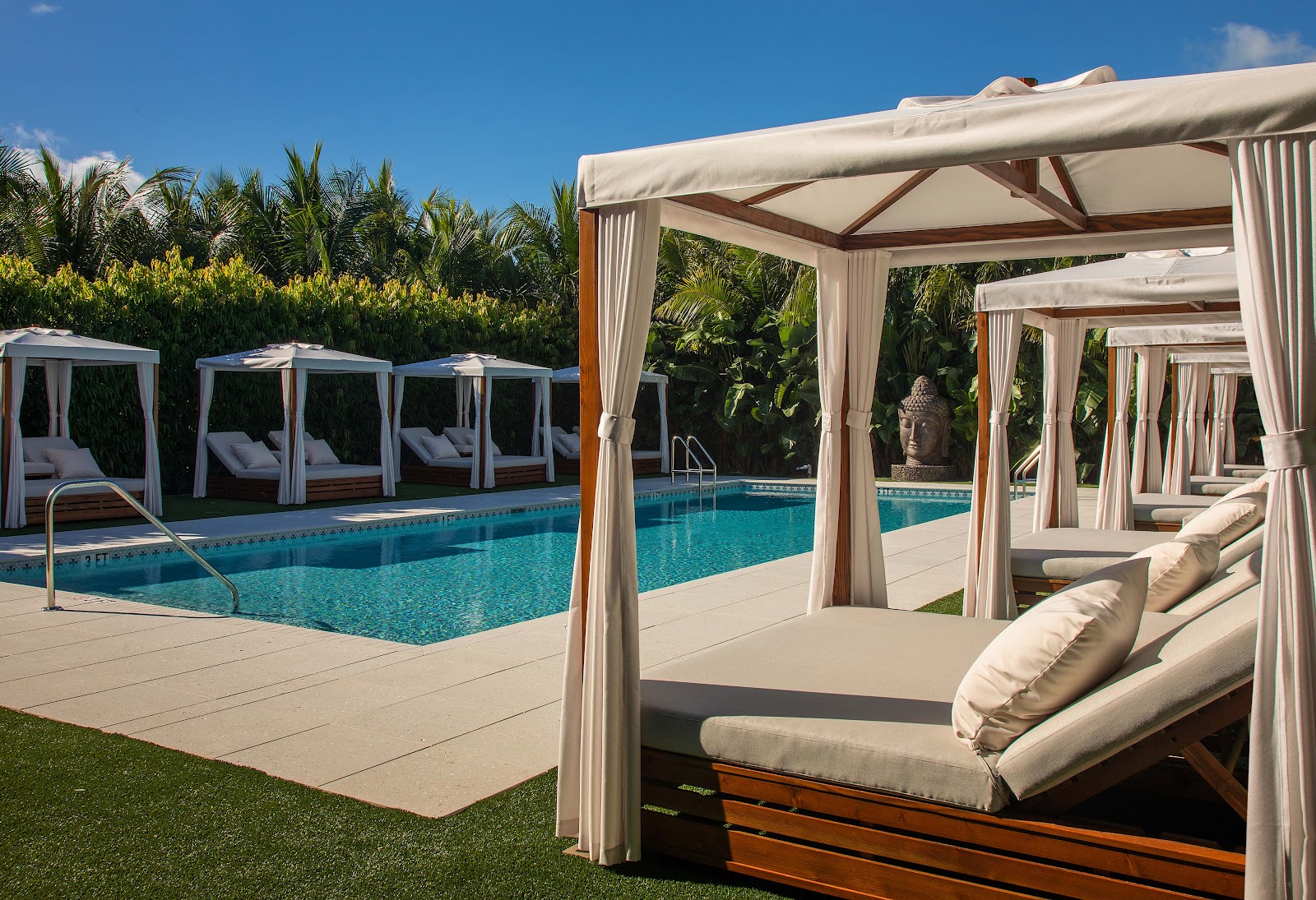 Beige cabana beds with curtains line the pool deck at Bungalows Key Largo, with palm trees and cabins visible beyond.