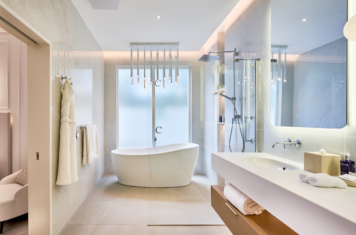 Modern bathroom with freestanding white tub, walk-in shower, dual vanity, and ocean views through large windows at Calabash Hotel.