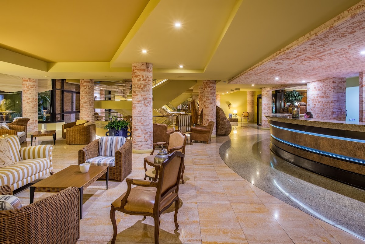 Lobby with yellow ceiling, brick columns, striped armchairs, and curved reception desk at Calheta Beach - All Inclusive - Savoy Signature.