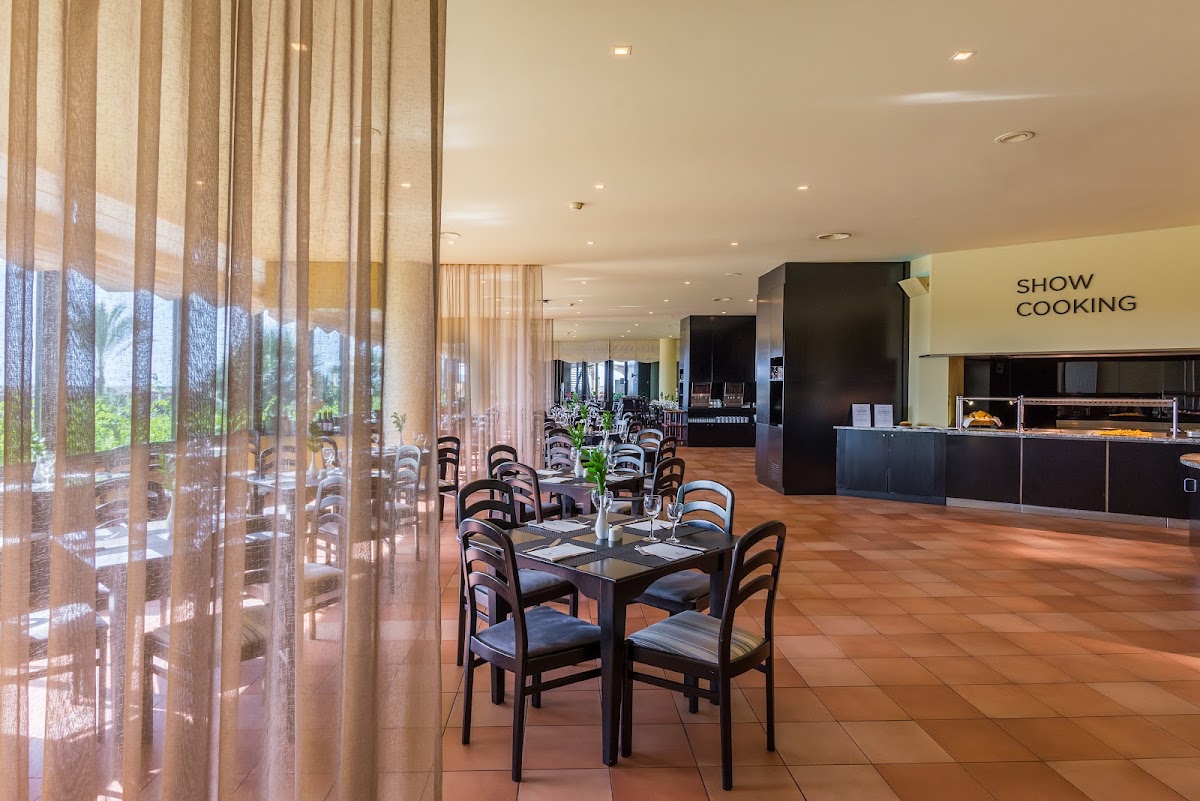 Dining room with black chairs at tables, sheer curtains, show cooking station, and terracotta tile floor at Savoy Signature.