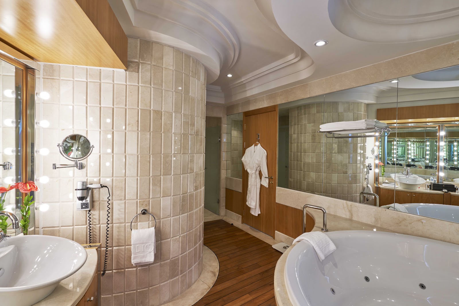 Luxury bathroom with curved shower enclosure, soaking tub, double vanity with lit mirror, and wood flooring throughout.