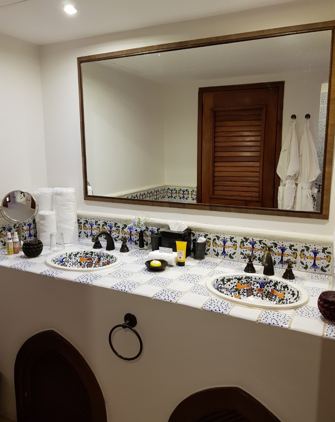 Bathroom vanity with dual sinks, patterned tile backsplash, large mirror, and black fixtures at Cap Maison Resort & Spa.
