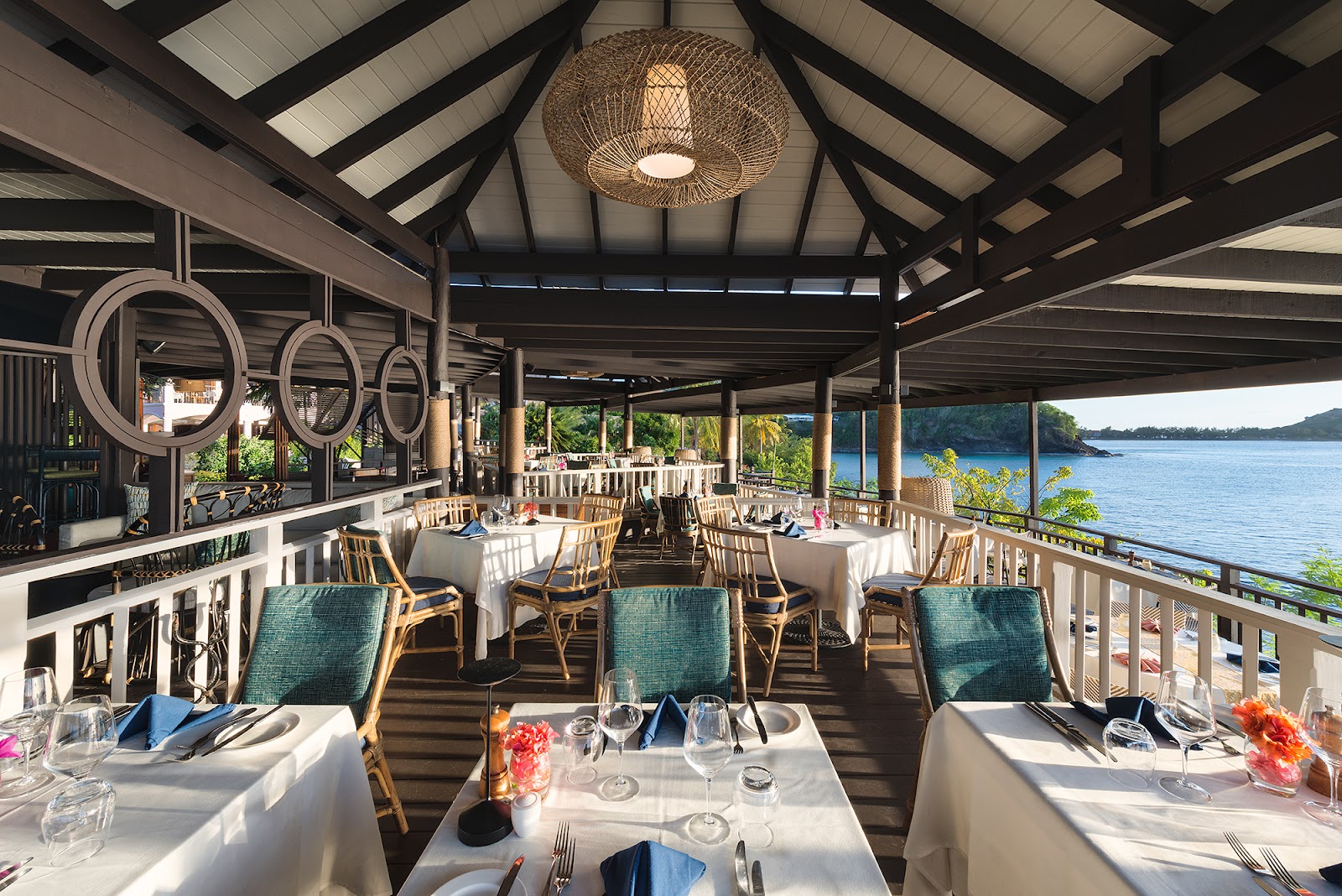 Dining room with white tablecloths and rattan chairs overlooking blue water and forested coastline at Cap Maison Resort & Spa.