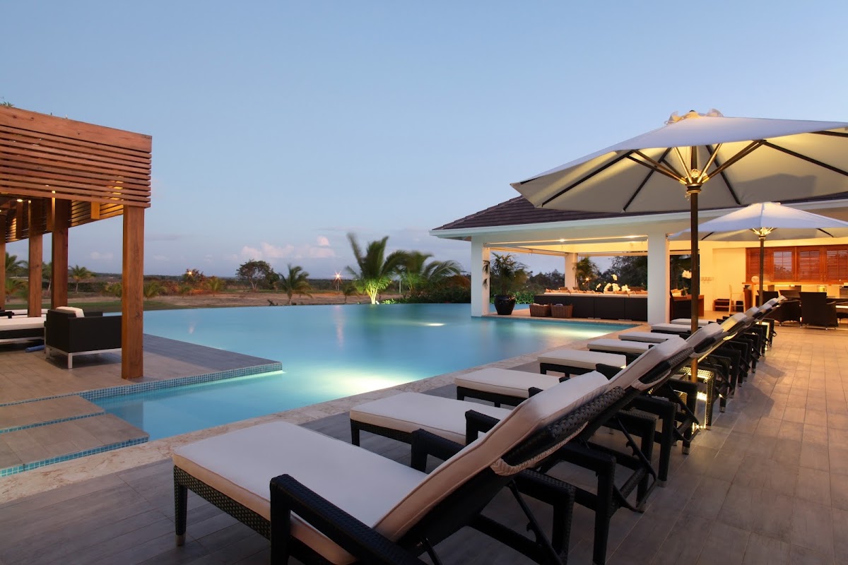 Row of lounge chairs with umbrellas facing the illuminated pool at Casa de Campo Resort & Villas at dusk.