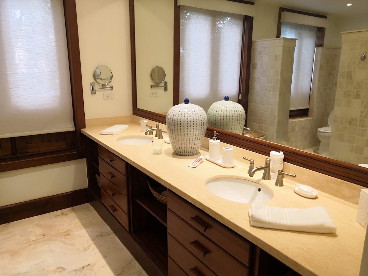 Double vanity bathroom with two round mirrors, decorative ceramic vessels, cream countertop, dark wood cabinets, and shower enclosure at Casa de Campo Resort & Villas.