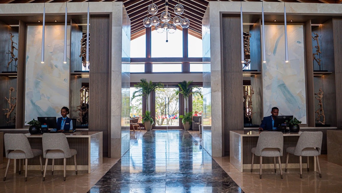 Modern lobby at Casa de Campo Resort & Villas with dual reception desks, soaring ceilings, pendant lights, and polished floors reflecting natural light.