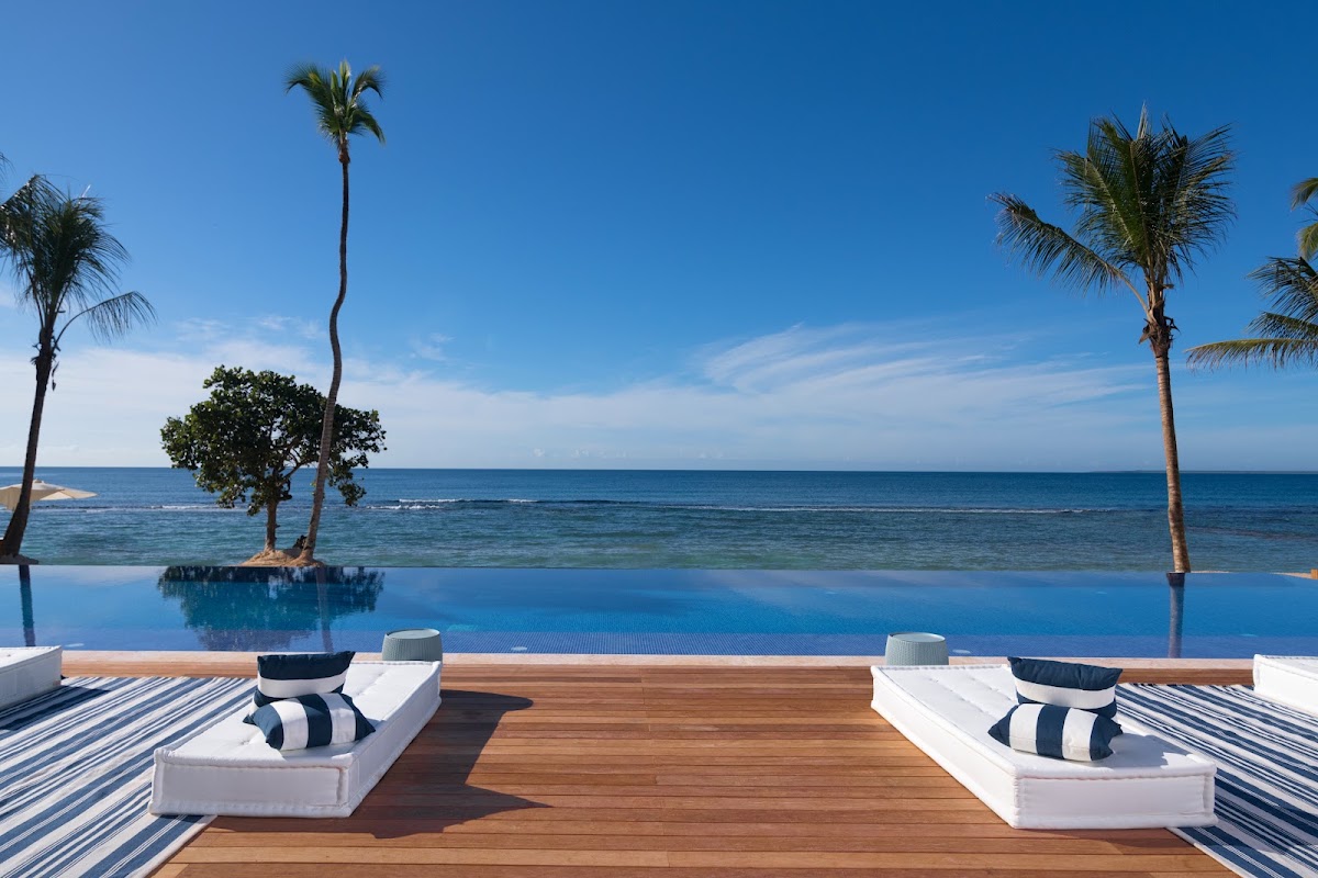 Infinity pool with loungers overlooking the ocean and palm trees at Casa de Campo Resort & Villas.