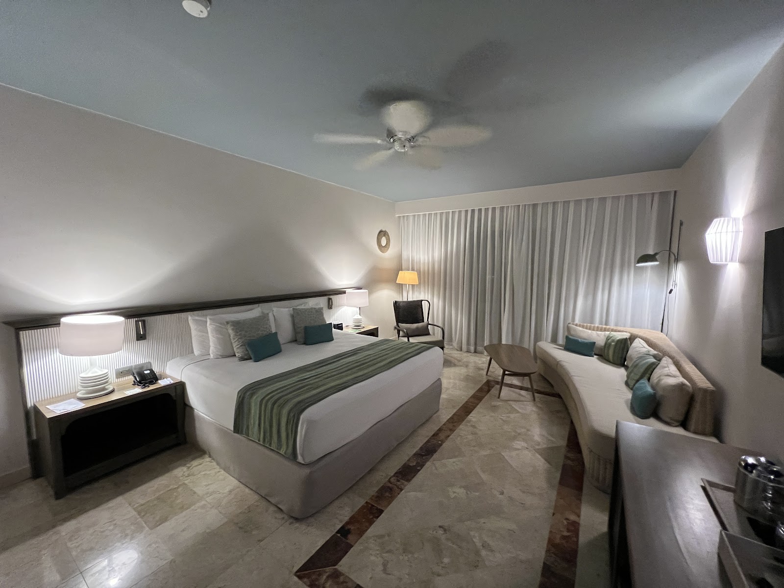 Spacious resort bedroom with king bed, seating area, neutral tones, and floor-to-ceiling curtains at Hotel Catalonia Royal Tulum.