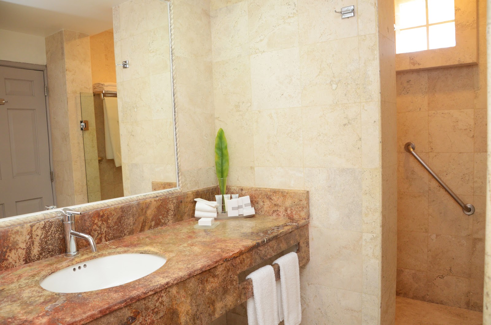 Resort bathroom with granite countertop, vessel sink, large mirror, and walk-in shower with travertine tile and grab bar.