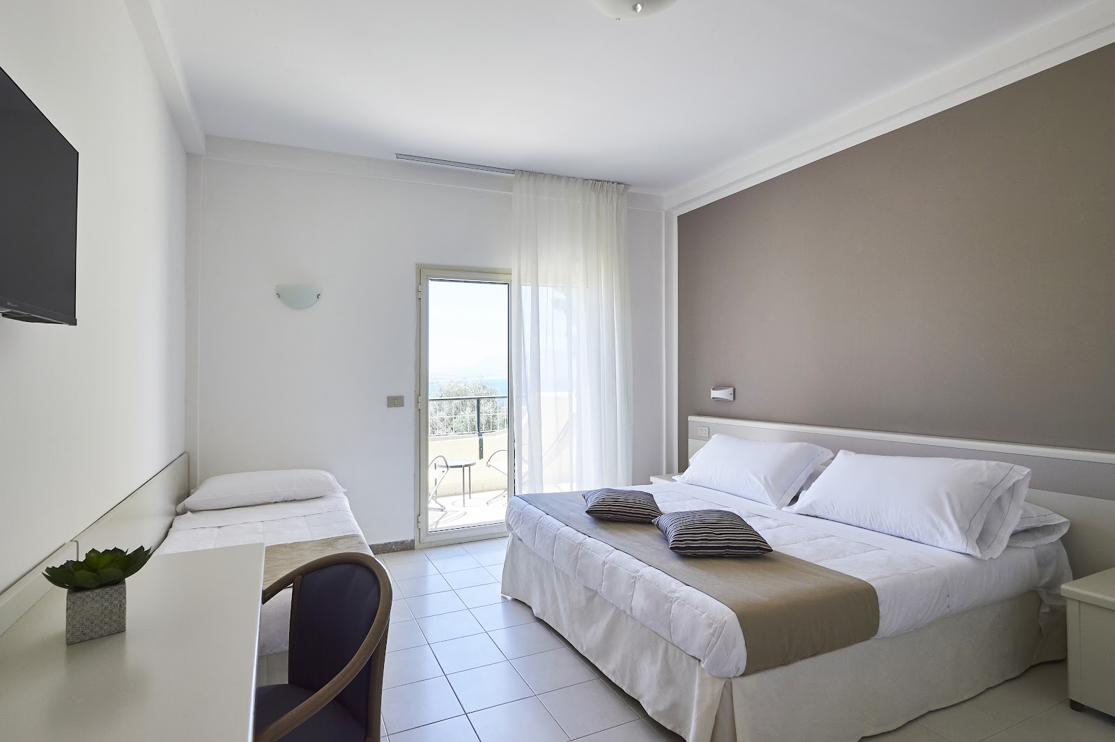 Resort bedroom with mustard yellow accent wall, white bedding, and open glass doors leading to a sea-view balcony.