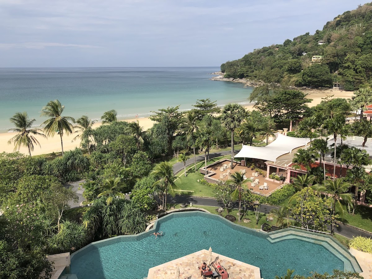 Centara Grand Beach Resort Phuket pool overlooking tropical beach with turquoise water, palm trees, and forested hillside.