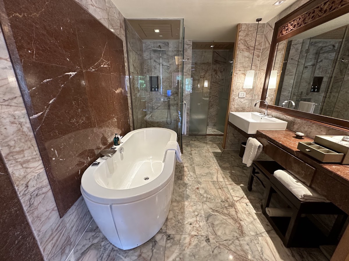 Luxury bathroom with marble walls, a freestanding soaking tub, walk-in shower with glass enclosure, and double vanity with wooden countertop.