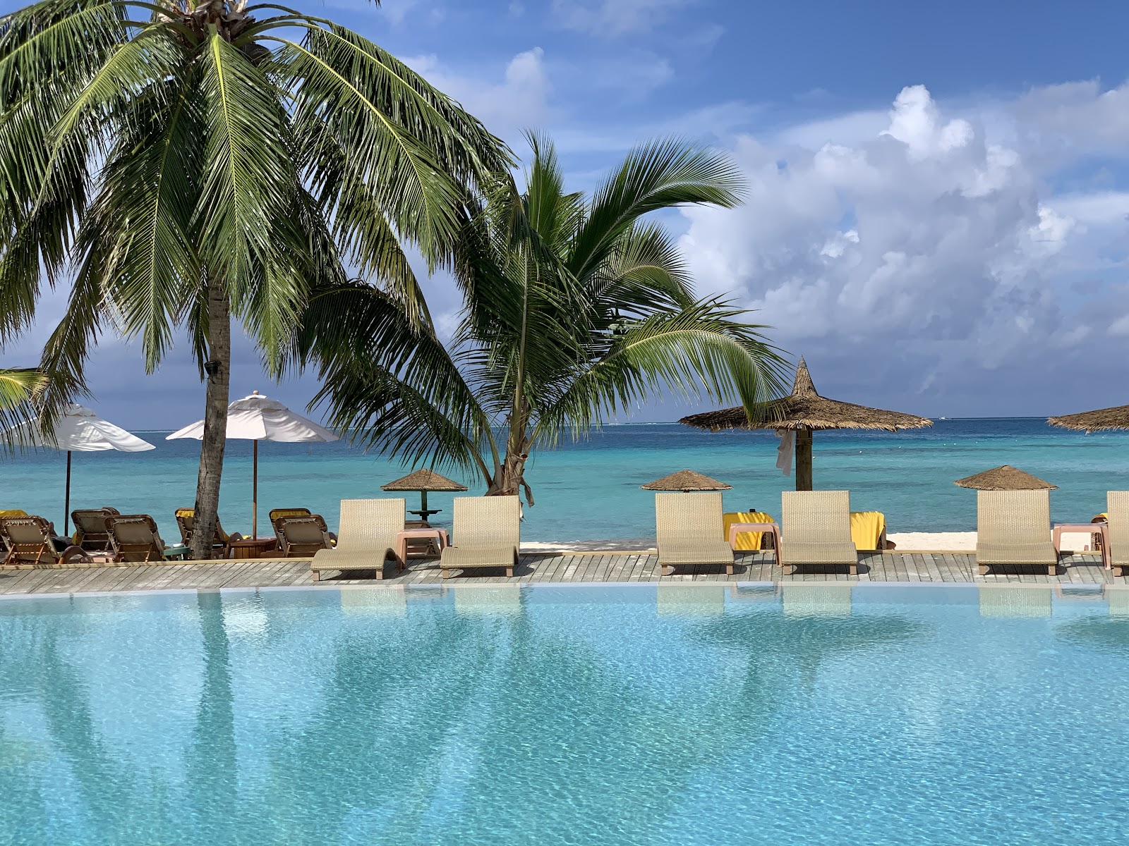 Pool deck with loungers and thatched umbrellas overlooking turquoise ocean and small islands at Centara Ras Fushi Resort & Spa Maldives.