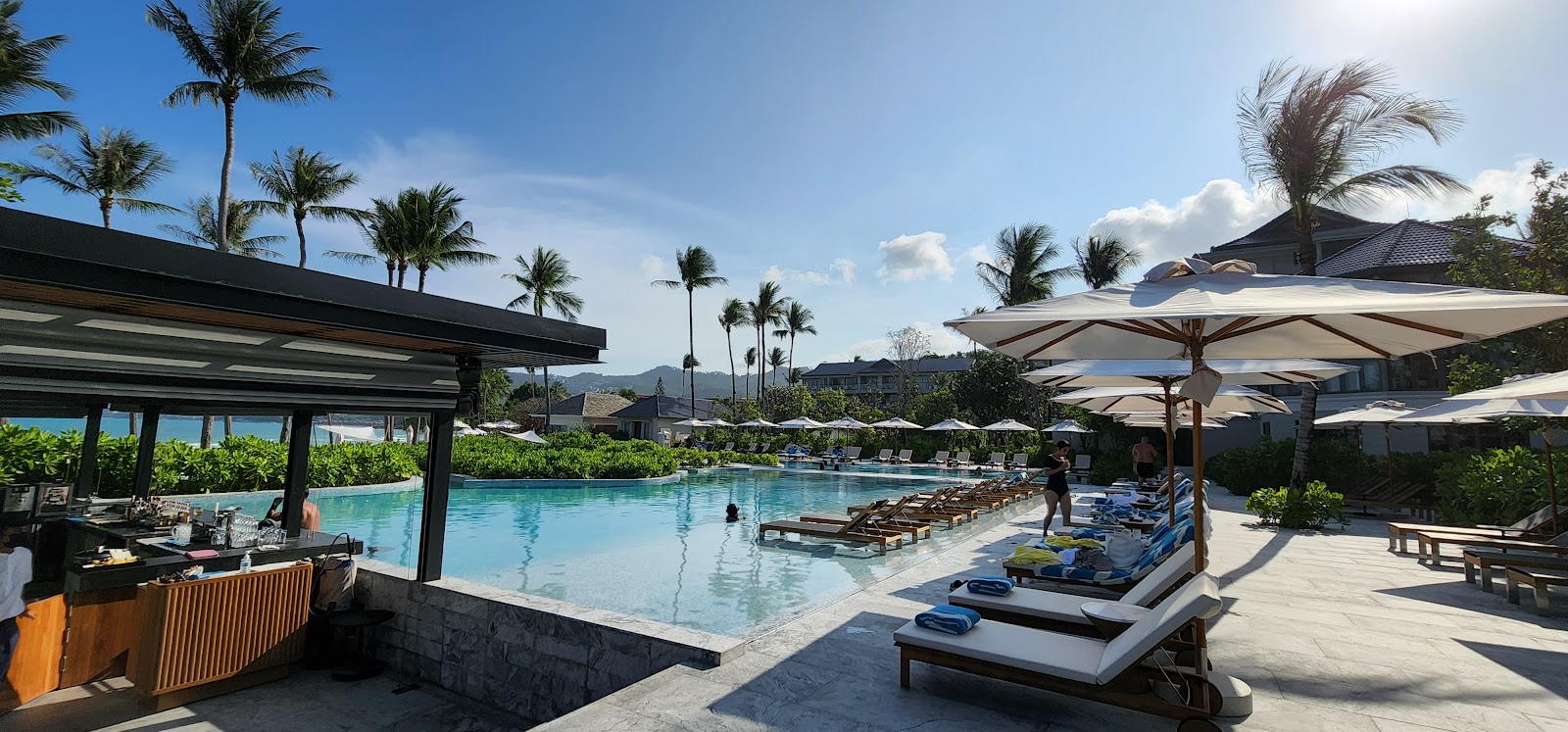 Oceanview pool at Centara Reserve Samui with lounge chairs, umbrellas, swim-up bar, and palm trees under clear sky.