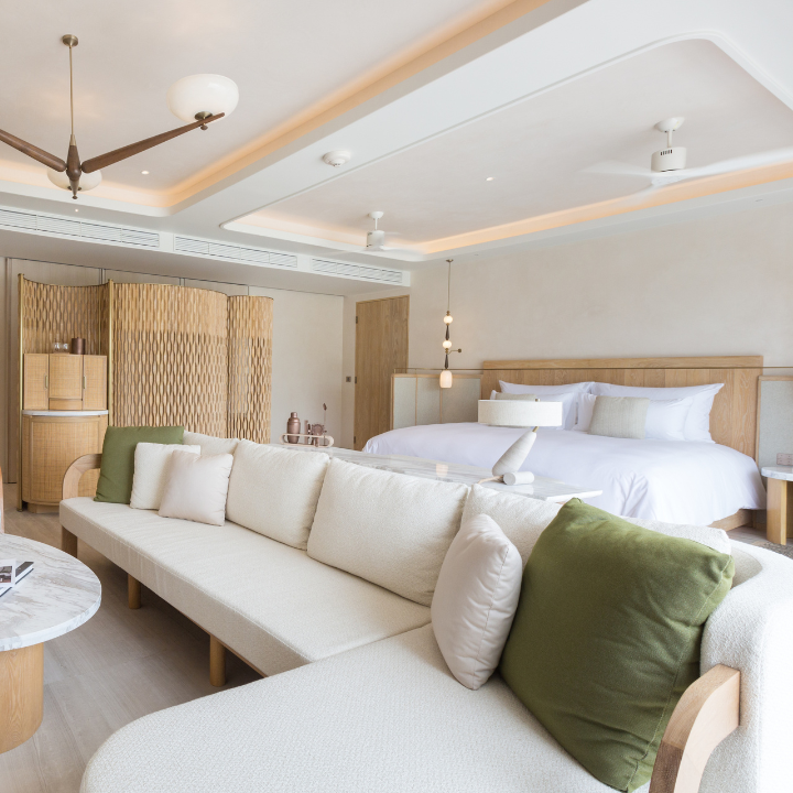 Centara Reserve Samui's curved pool complex with white loungers overlooks a sandy beach lined with palm trees and turquoise water.