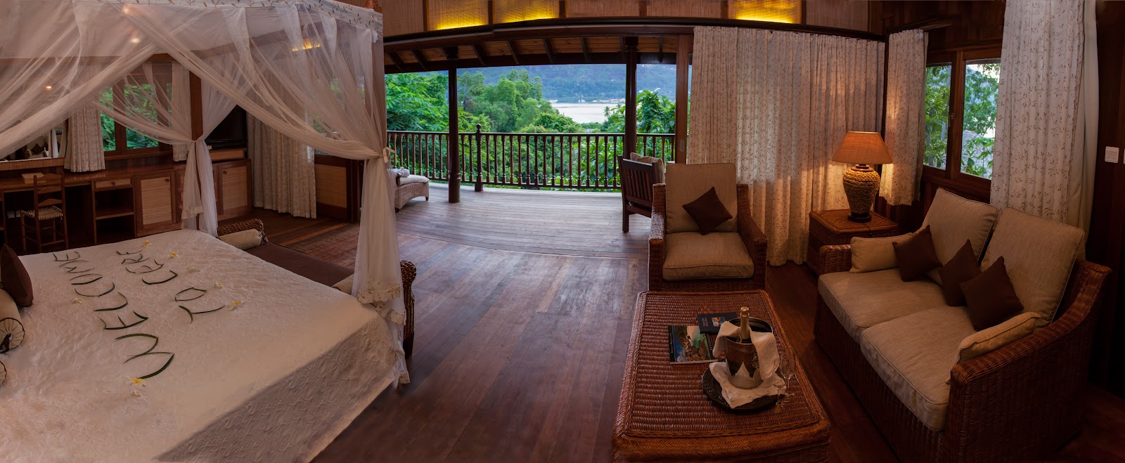 Tropical beachfront resort with blue pool, white umbrella, and thatched-roof structures nestled among palm trees and boulders on sandy grounds.