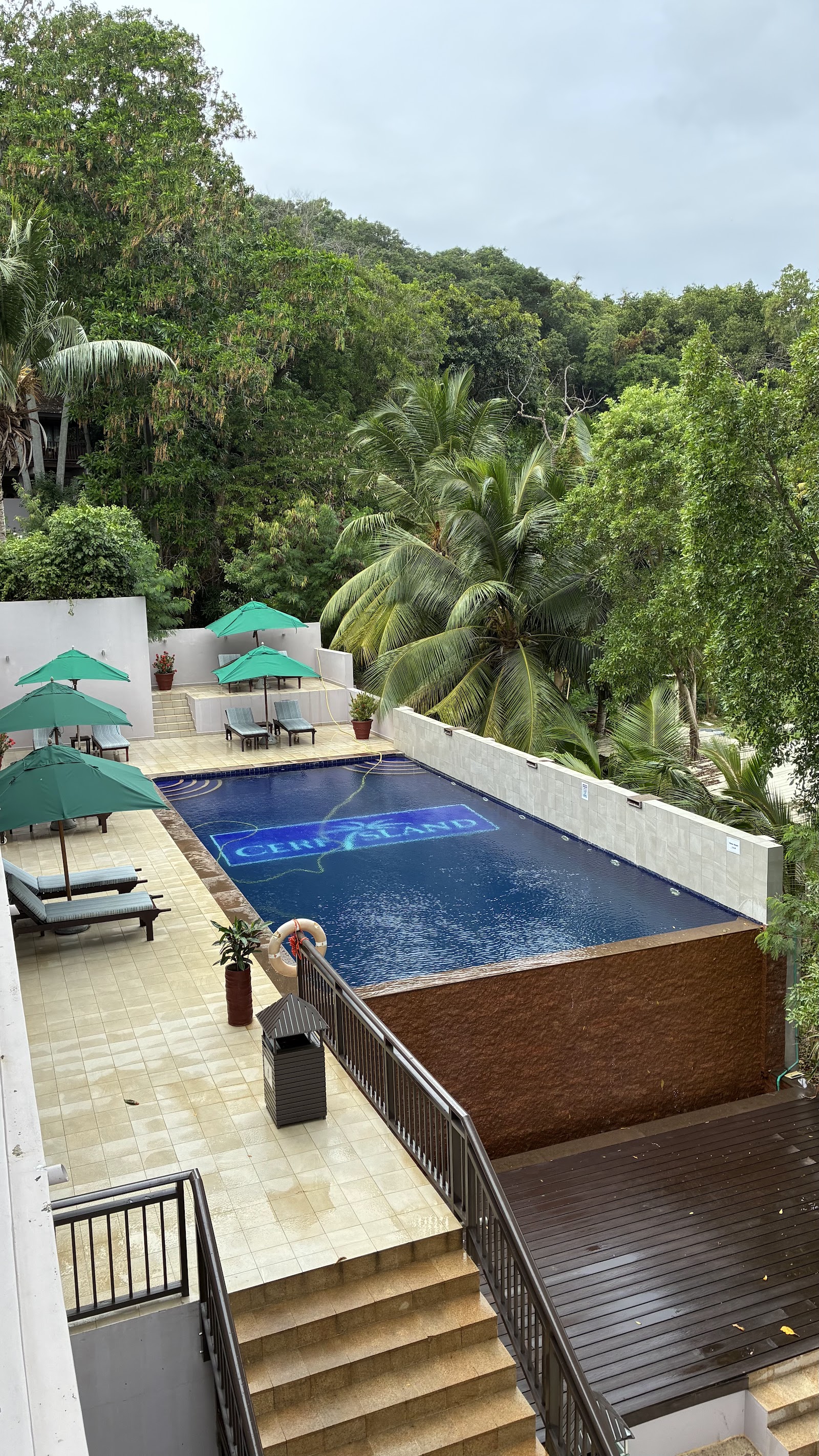Spacious resort suite with canopied bed, seating area, and wooden deck overlooking forested hillside and distant ocean.