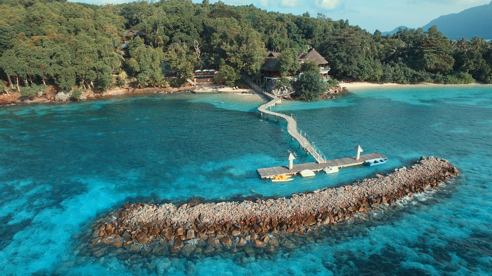 Yellow kayak in foreground on calm water at sunset, with volcanic island, wooden structures, and forested coastline at Cerf Island Resort.