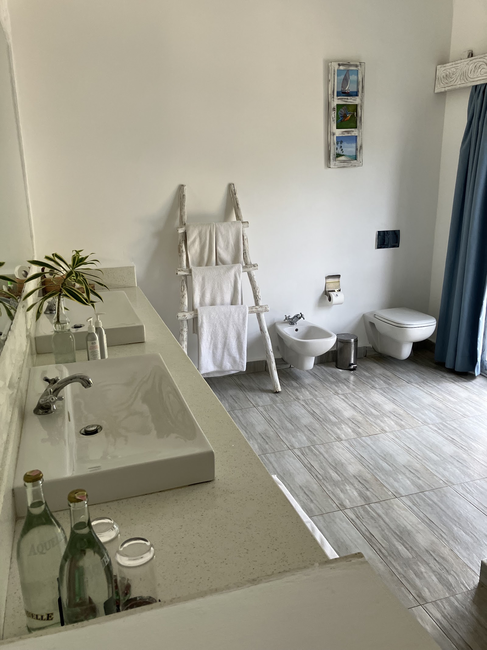 Modern resort bathroom with white sink, bidet, toilet, towel ladder, and gray tile flooring at Chale Island Resort.