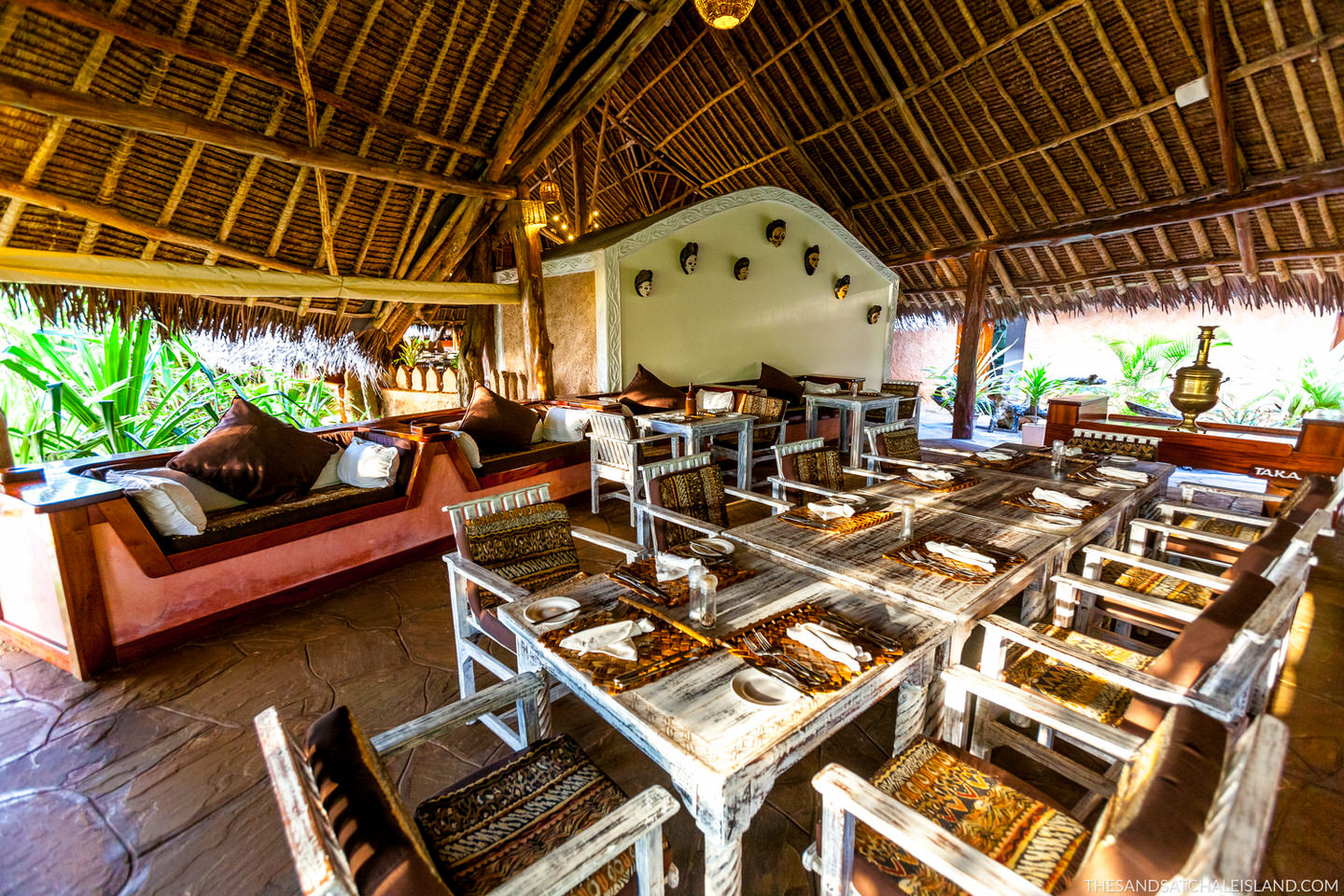 Open-air dining pavilion with thatched roof, wooden beams, red banquette seating, and whitewashed tables at Chale Island Resort.