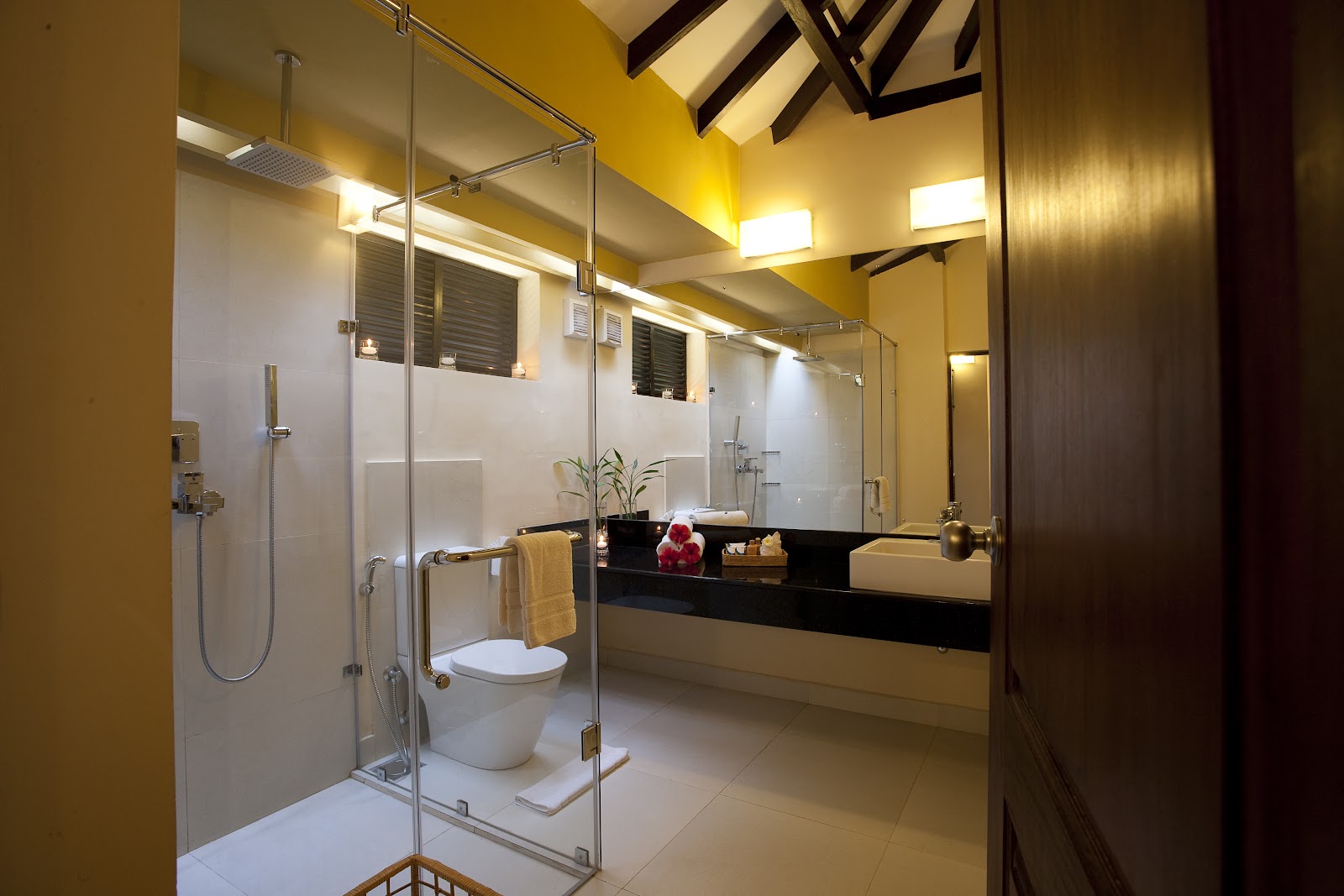 Bathroom with dual white vessel sinks on black countertop, illuminated mirrors, shower area, and toiletries at Club Hotel Dolphin.