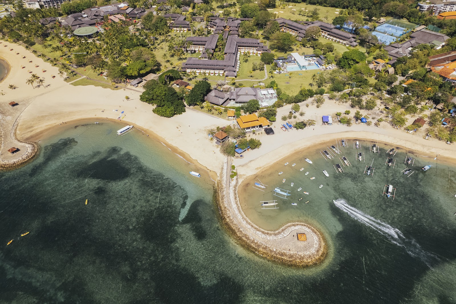 Aerial view of Club Med Bali's twin sandy beaches with traditional bungalows nestled among tropical trees and green lawns inland.