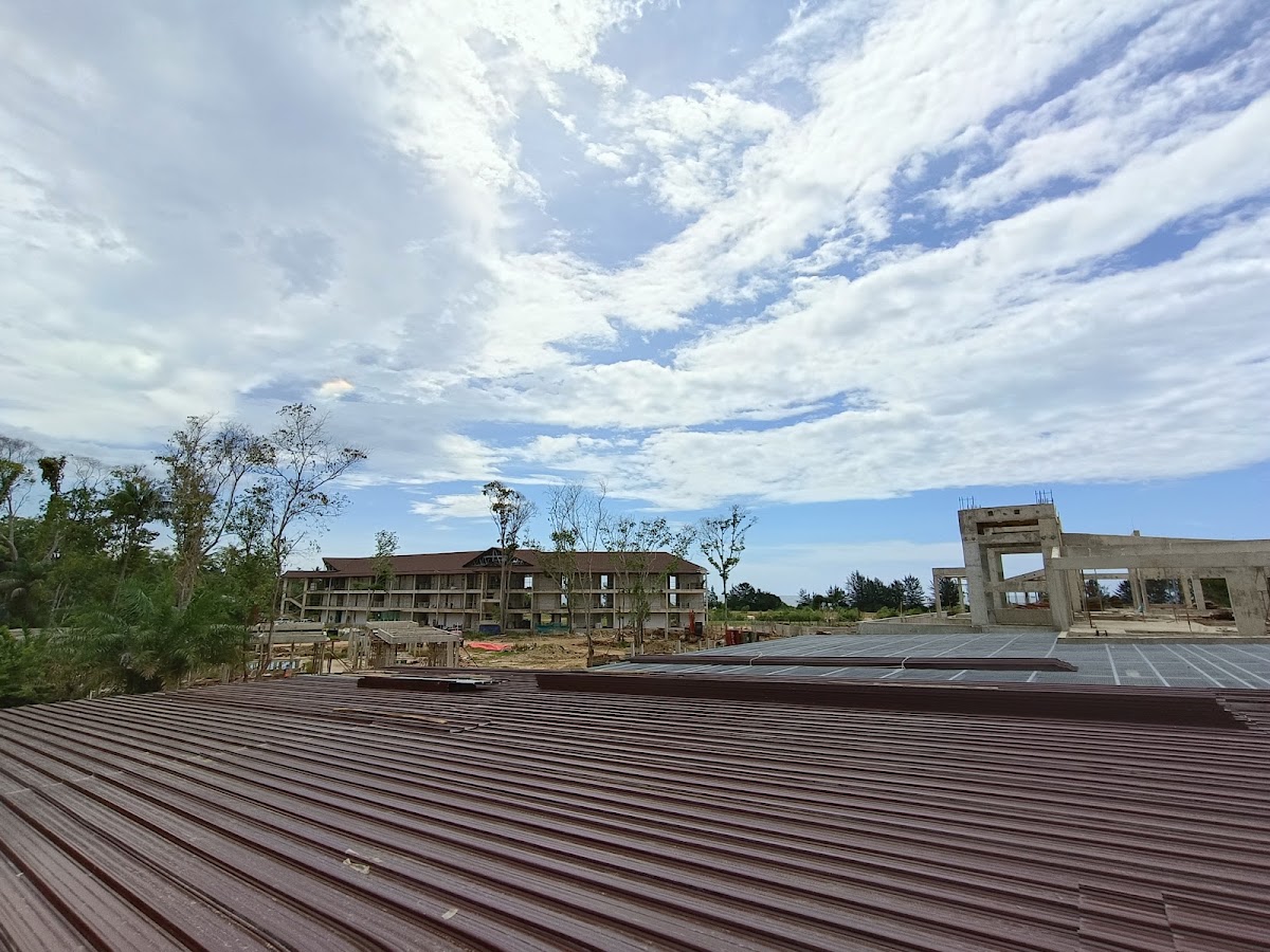 Construction site at Club Med Borneo with metal roofing in foreground, unfinished concrete structures, and sparse vegetation under cloudy sky.