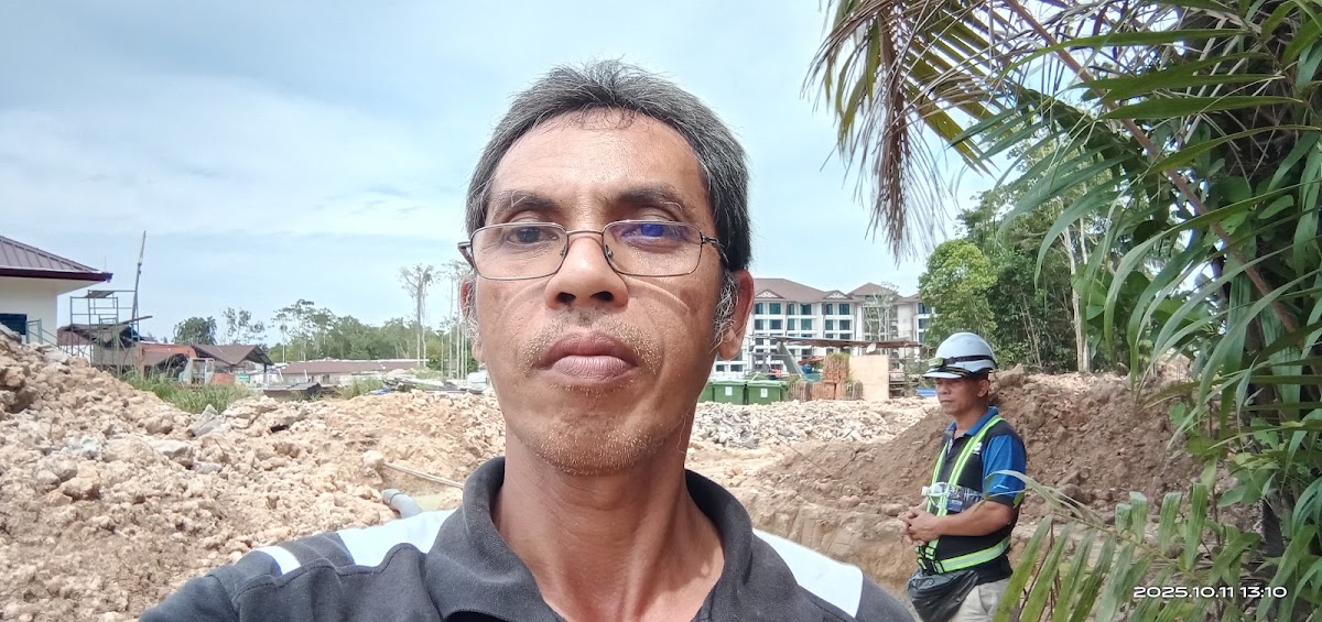 Man in glasses and hard hat standing on construction site with resort buildings visible in background.