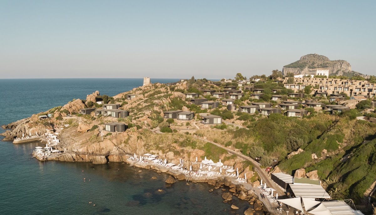 Modern bungalows cascade down a rocky hillside toward turquoise Mediterranean waters at Club Med Cefalù in Sicily.