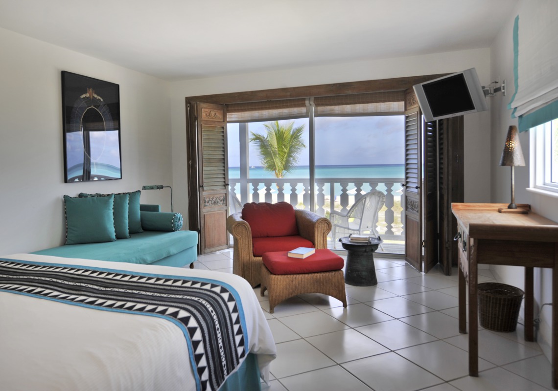 Resort room with bed, turquoise sofa, red armchair, and ocean view through balcony doors at Club Med Columbus Isle.