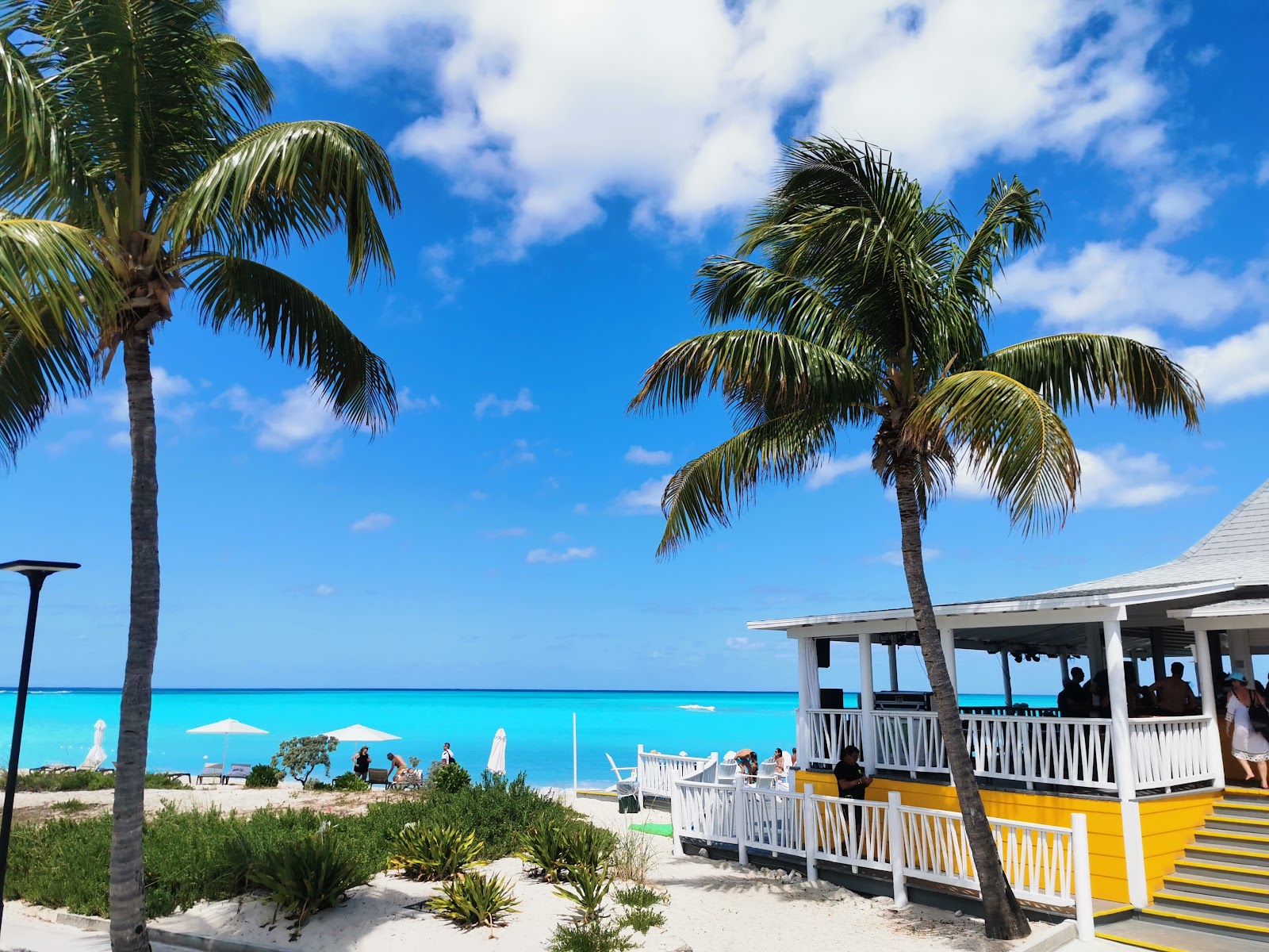 Turquoise waters and white sand beach at Club Med Columbus Isle, with rocky shoreline in foreground and resort buildings visible along the shore.