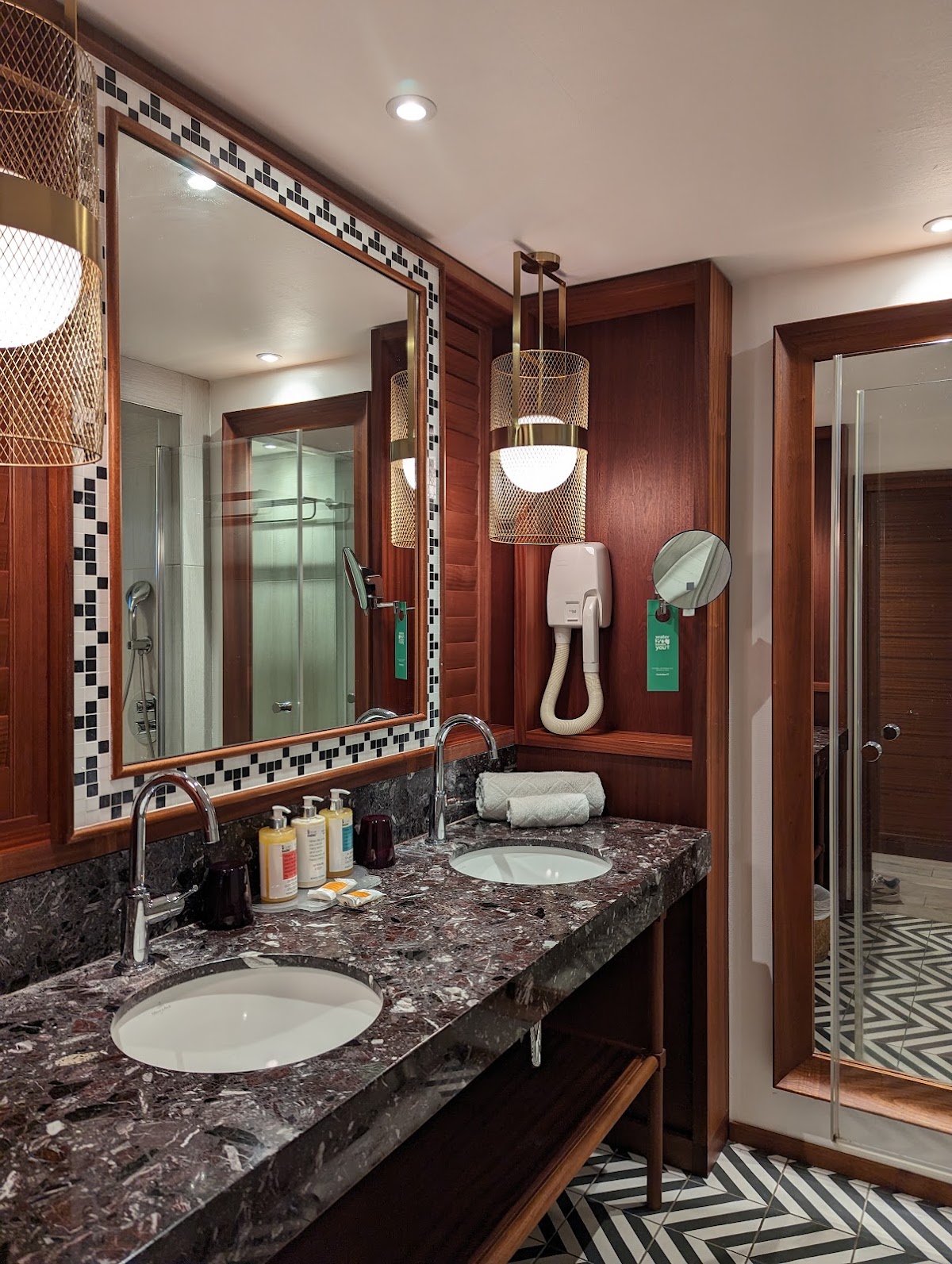 Bathroom with dark granite countertop, dual sinks, large mirror with wood frame, shower visible left, and woven pendant light fixture.