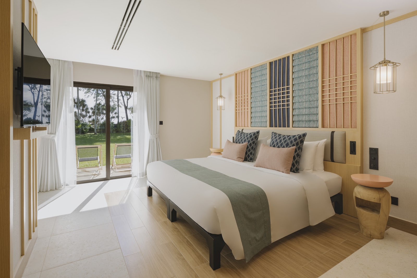 Resort guest room with king bed, wooden headboard wall art, and glass doors opening to lawn and palm trees.