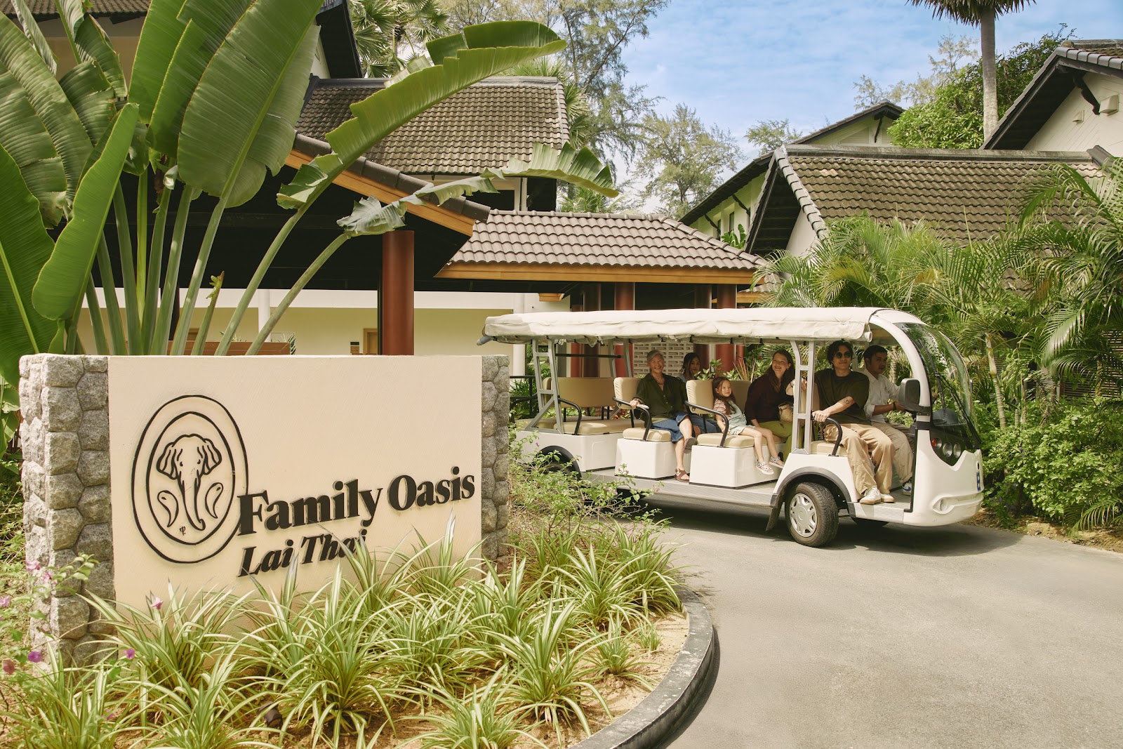 Multi-generational family walks across manicured lawn surrounded by tall palm trees and white resort buildings under clear sky.