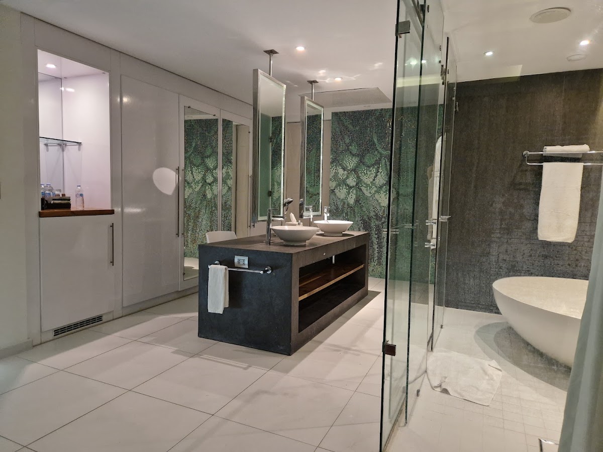 Modern bathroom with dark vanity, dual vessel sinks, green tile accents, walk-in shower, soaking tub, and recessed lighting throughout.