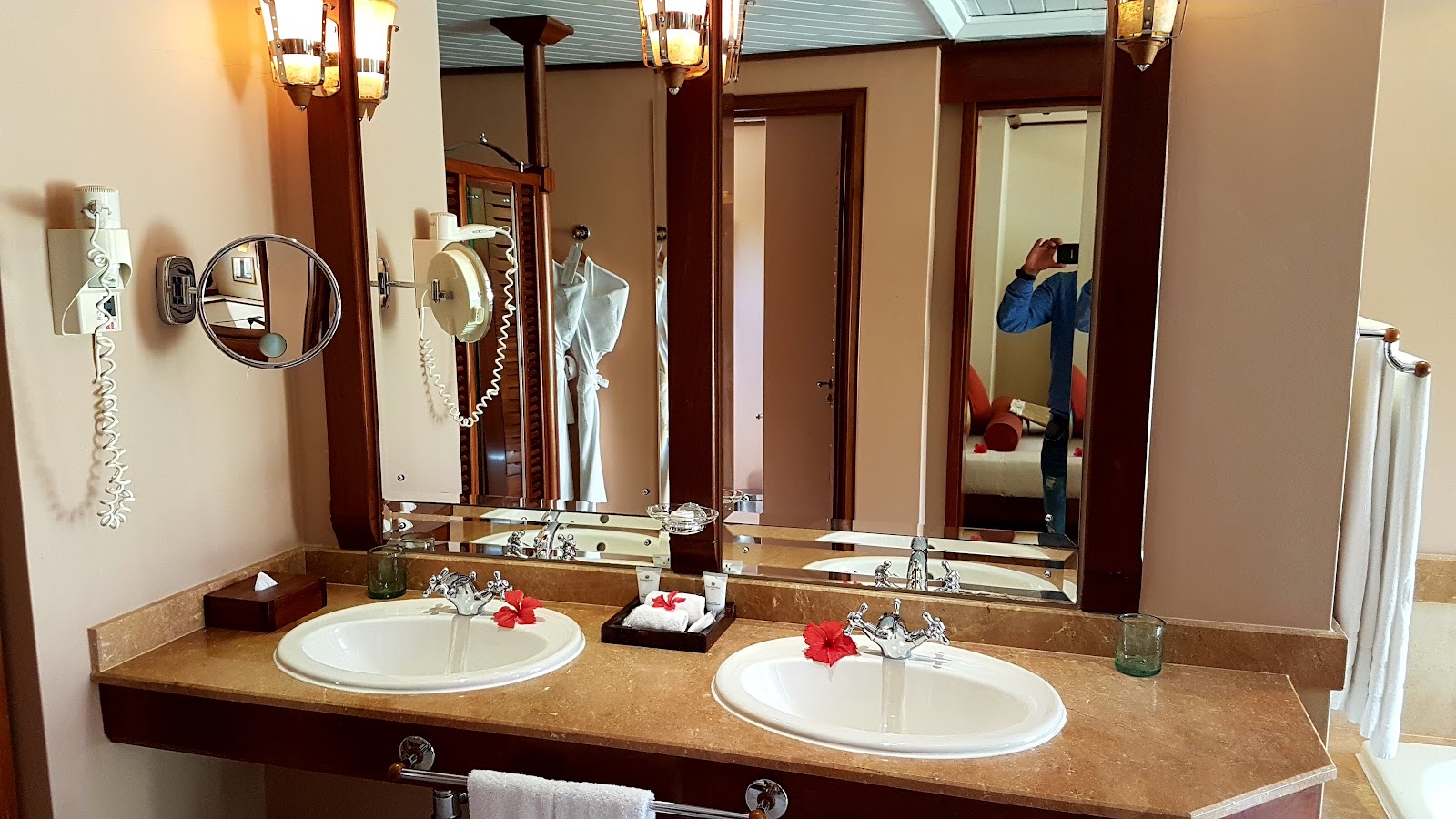 Dual vanity sink with brown countertop and red flowers, large mirrors, and wood-trimmed walls in a resort bathroom.