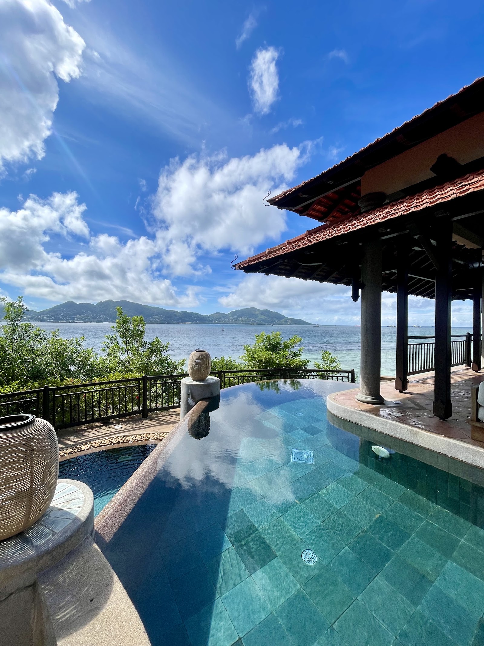Infinity pool with stone sculpture overlooks turquoise ocean and forested islands under blue sky at Club Med Seychelles.