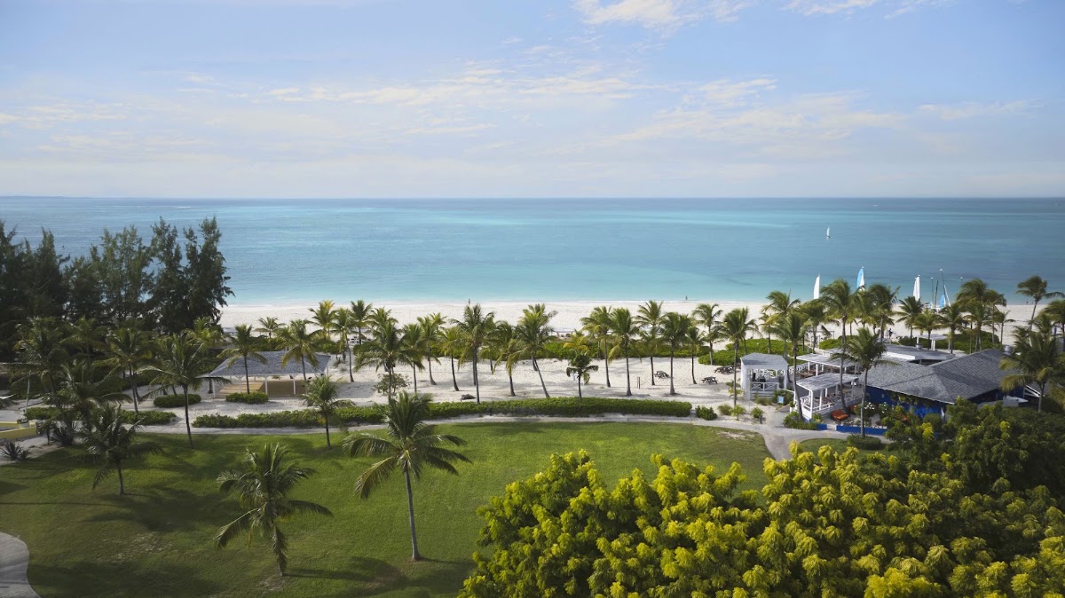 Club Med Turkoise beachfront with turquoise water, white sand, palm trees, manicured lawn, and beach facilities under clear sky.