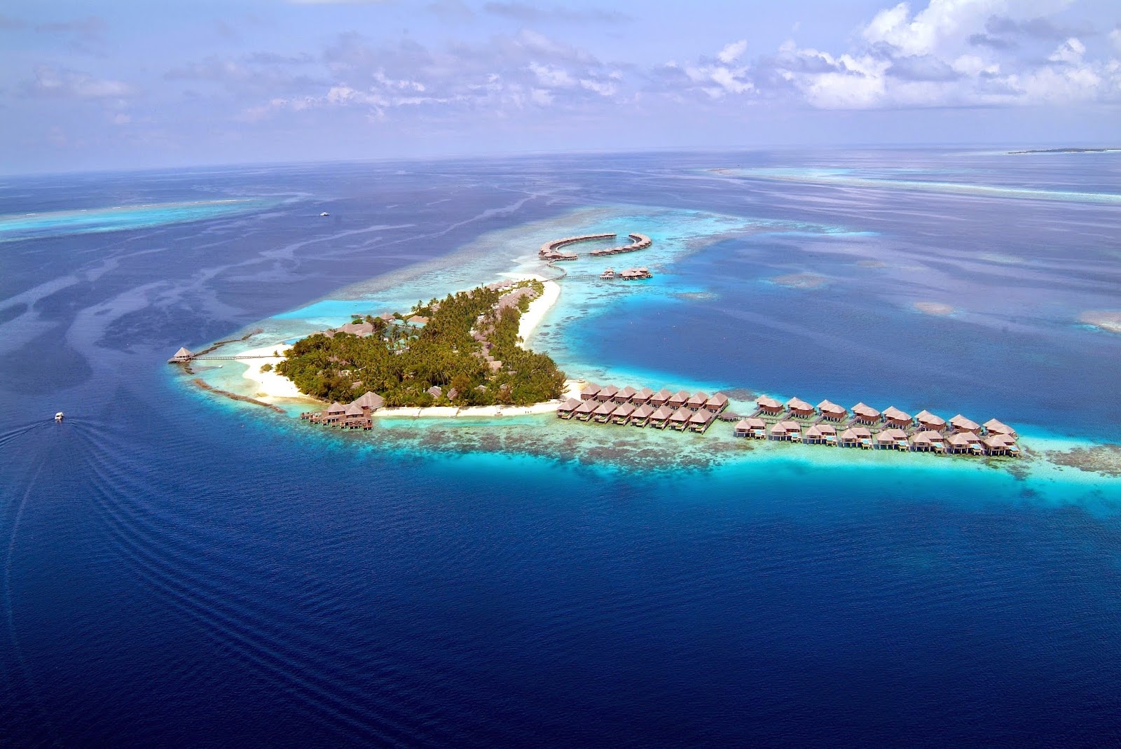 Aerial view of Coco Bodu Hithi's island resort with overwater bungalows, white-sand beach, and dense tropical vegetation surrounded by turquoise lagoon and deep blue ocean.