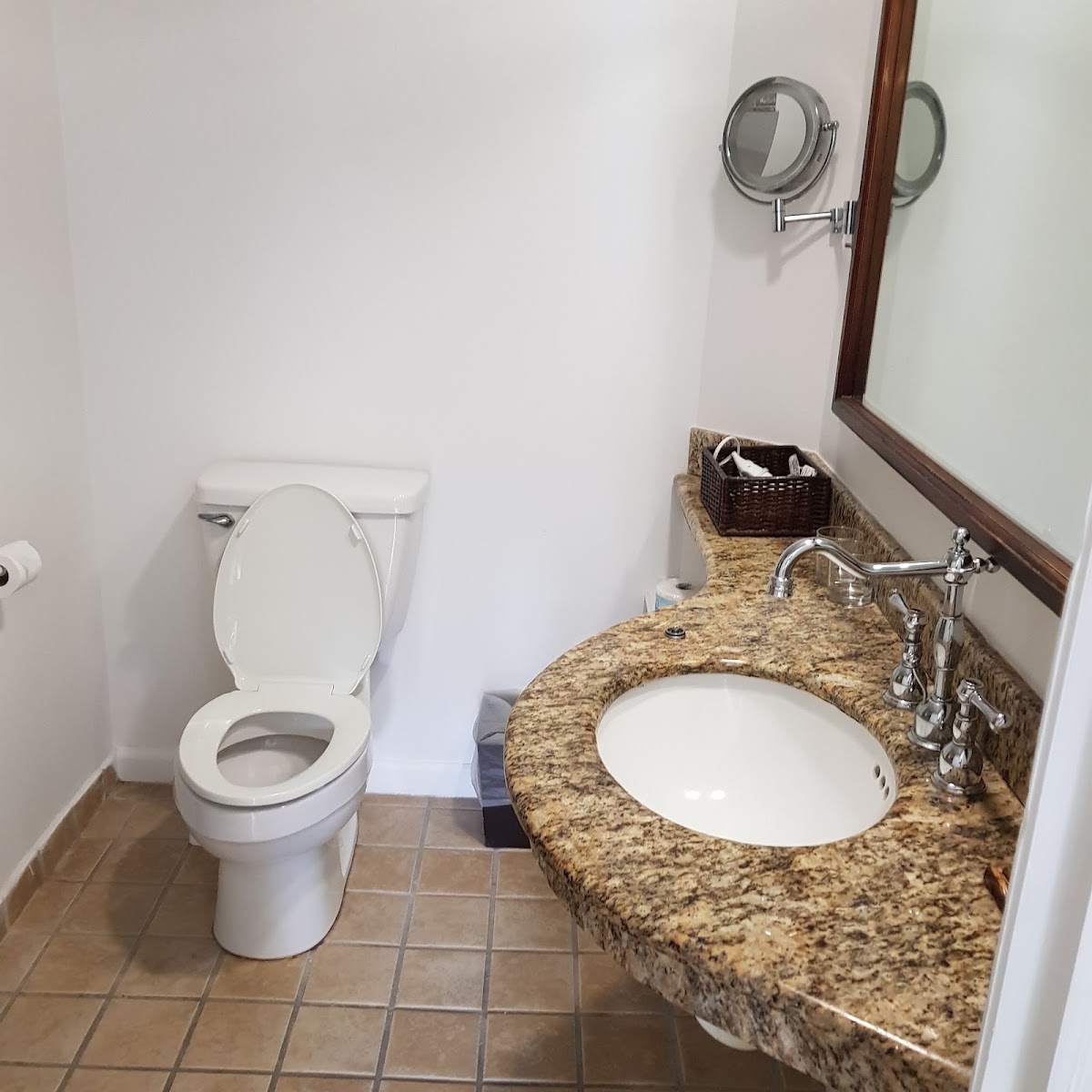 Resort bathroom with granite countertop, single sink, chrome faucet, wall mirror, and toilet on tiled floor.